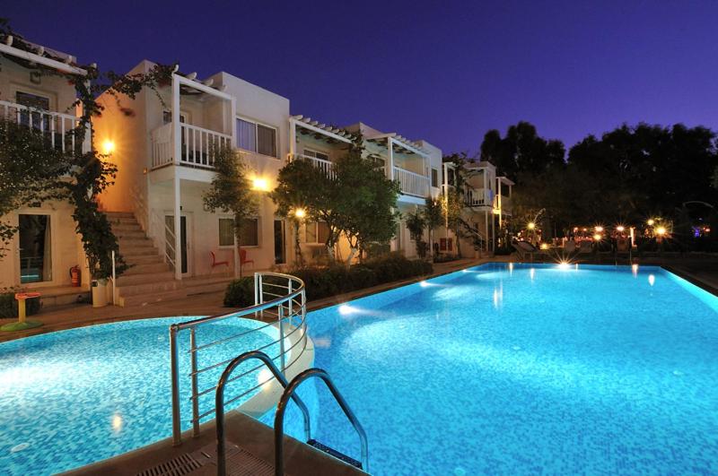a large swimming pool in front of buildings at night at Hotel Gumusluk in Gumusluk