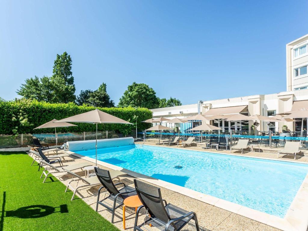 a swimming pool with chairs and umbrellas next to a building at Novotel Bourges in Bourges