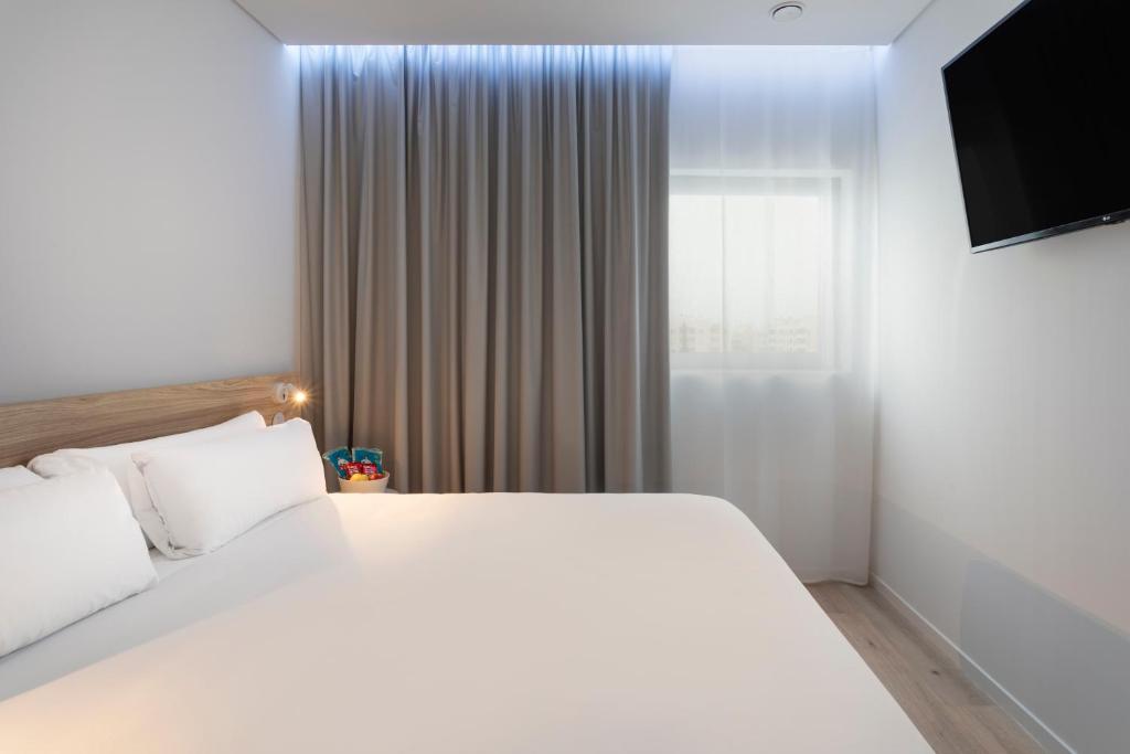a bedroom with a large white bed and a television at B&B HOTEL Olhão Algarve in Olhão