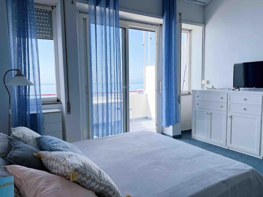a bedroom with a bed with blue curtains and a large window at Cielo e Mare in Scalea