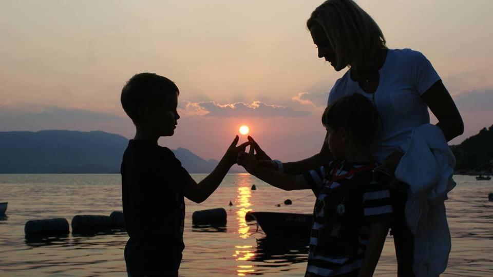 a boy and a woman holding hands with the sunset in the water at AG Komarna - Peljesac Bridge Apartments in Komarna