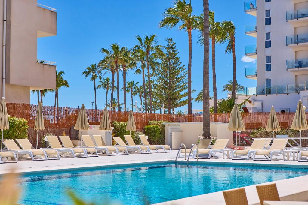 basen z krzesłami i parasolami oraz palmami w obiekcie Universal Hotel Bikini w Cala Millor