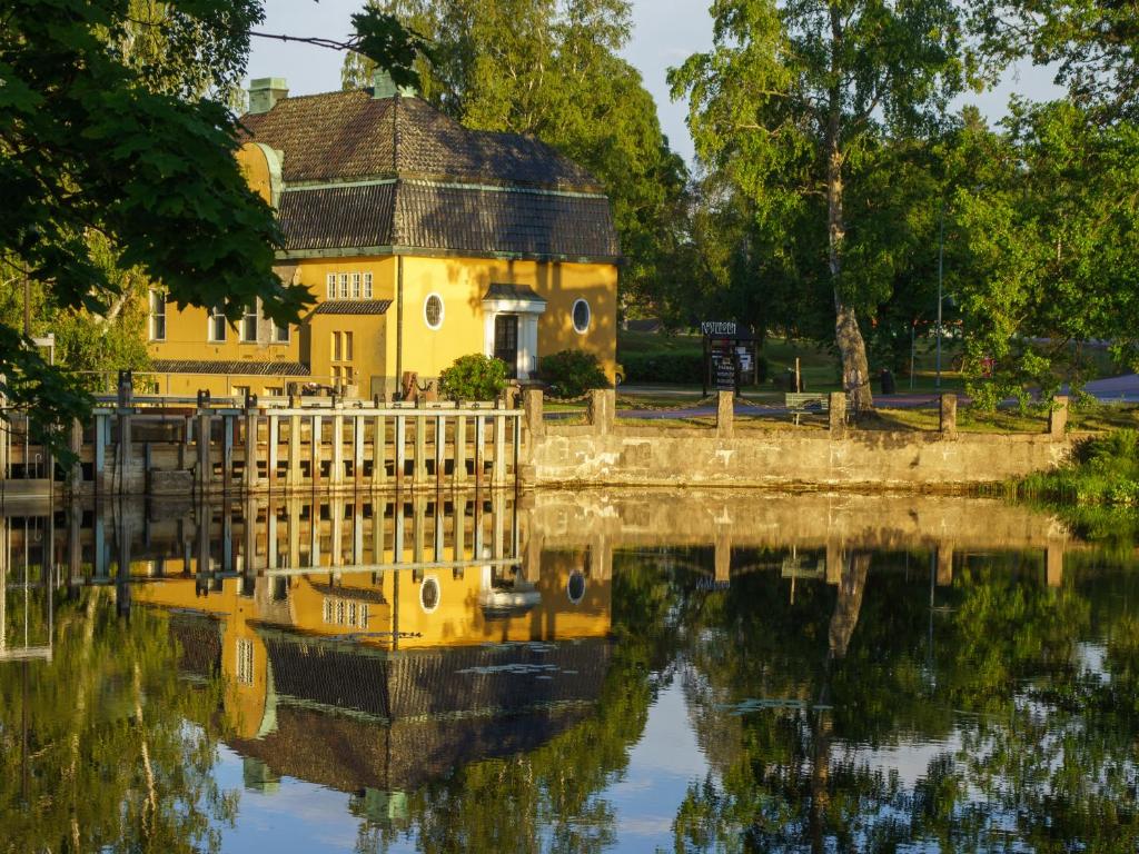 una casa amarilla se refleja en un cuerpo de agua en Kustleden Vandrarhem, en Strömsbruk