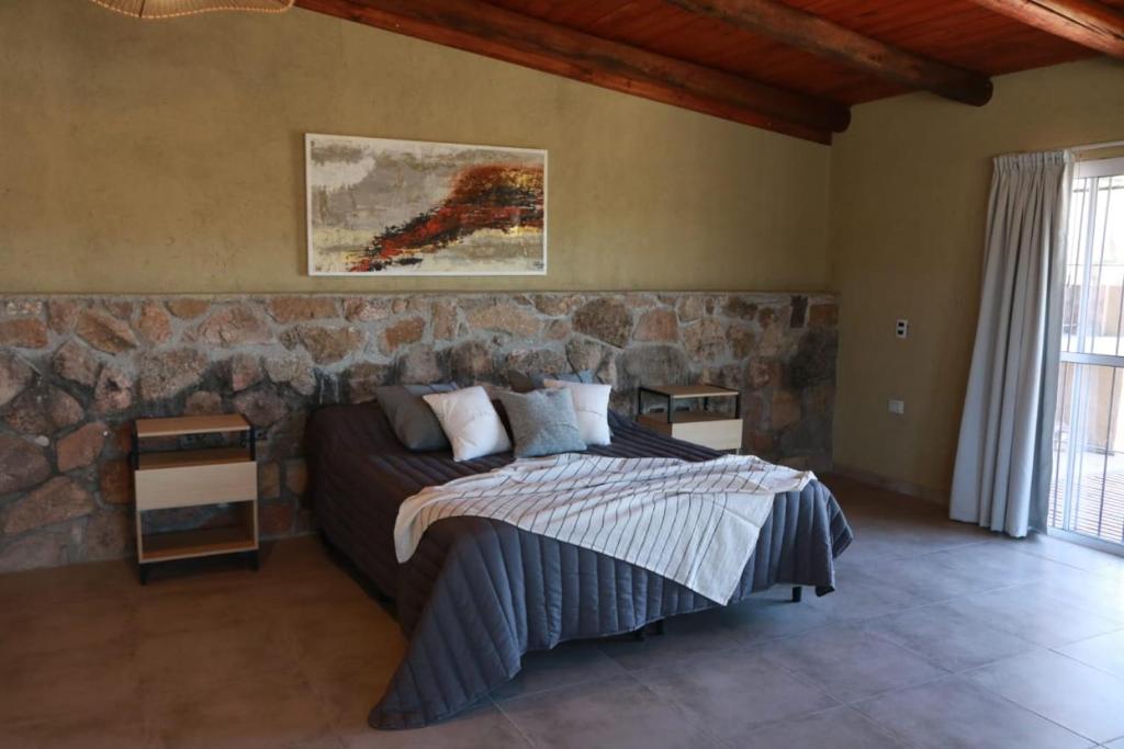 1 dormitorio con cama y pared de piedra en Cabañas Tío Joe en San Antonio de Arredondo