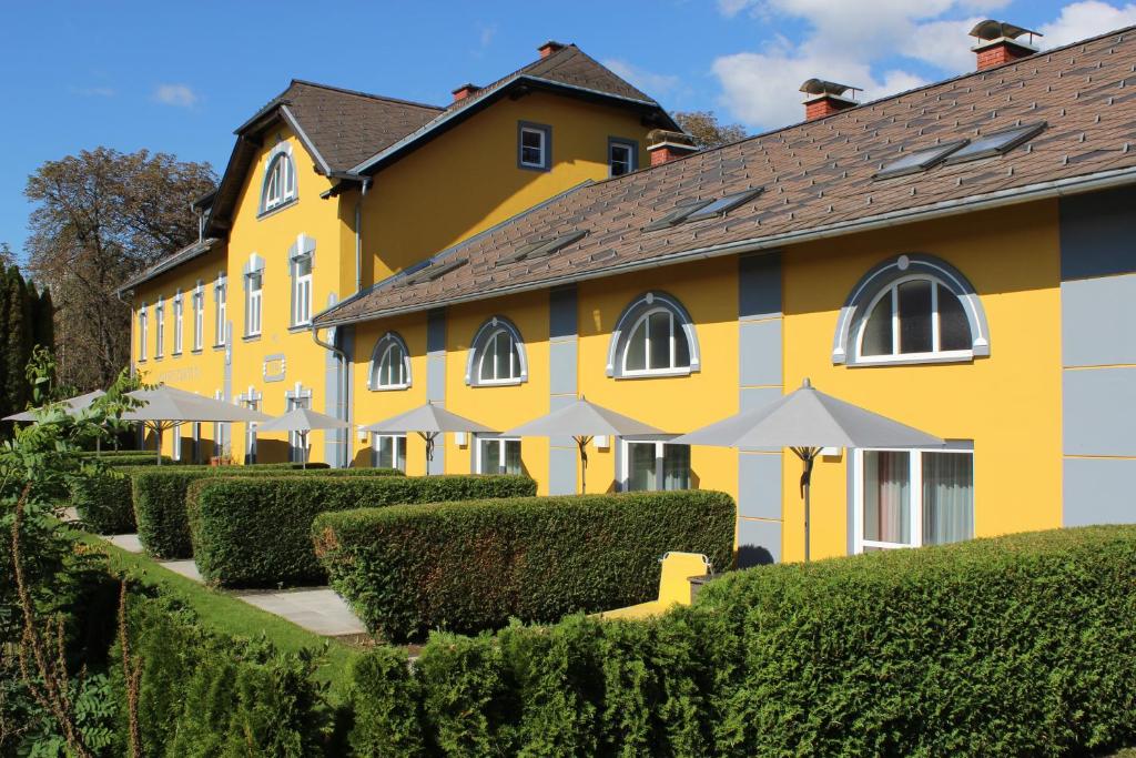 um edifício amarelo com arbustos e guarda-chuvas à sua frente em Gästehaus Karl August em Fohnsdorf