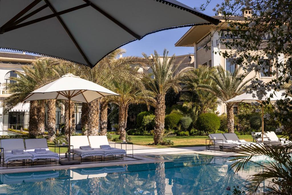 a pool with chairs and umbrellas next to a building at Palais Ronsard Relais & Chateaux in Marrakech