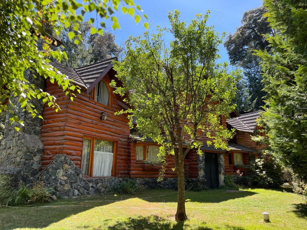 ein Blockhaus mit einem Baum davor in der Unterkunft Cuncumen Casa de Montaña in Villa La Angostura