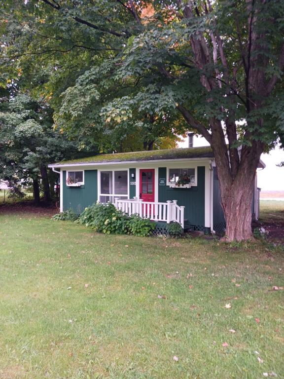a green house with a red door and a tree at Maison Marcotte in Saint-Michel