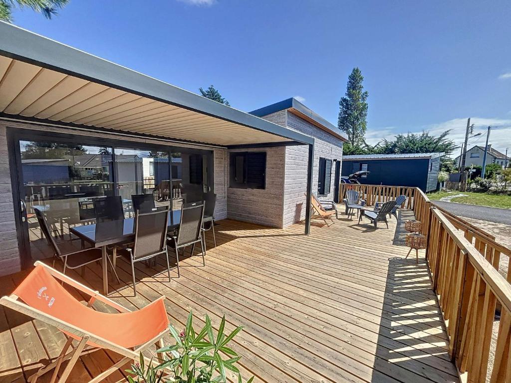 une grande terrasse en bois avec des chaises et une table dans l'établissement Chalet à Jullouville - 6 couchages, piscine chauffée, près de la plage et commerces - FR-1-361-523, à Jullouville