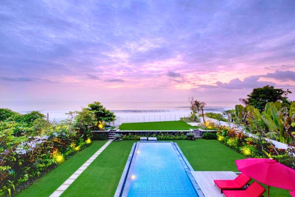 a backyard with a swimming pool and lawn with umbrellas at Angkasa 5 BR Beachfront Villa JU31 in Keramas