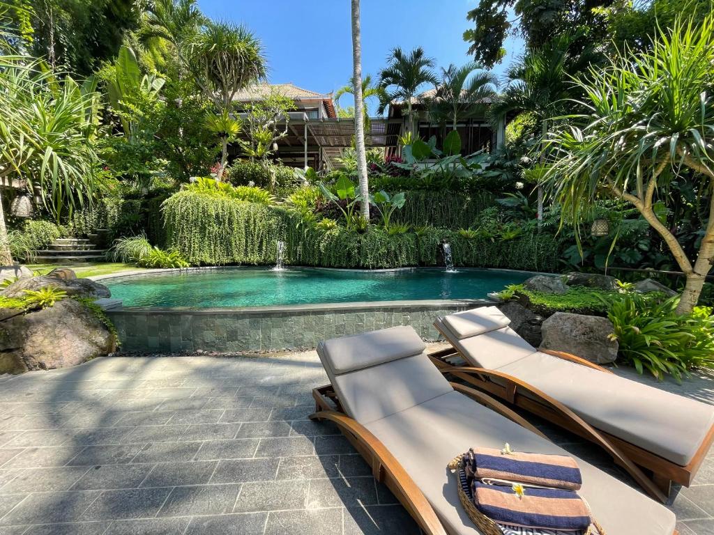 une piscine avec deux chaises longues devant dans l'établissement The Ubāri Bali - Luxury Riverside Escape, à Ubud