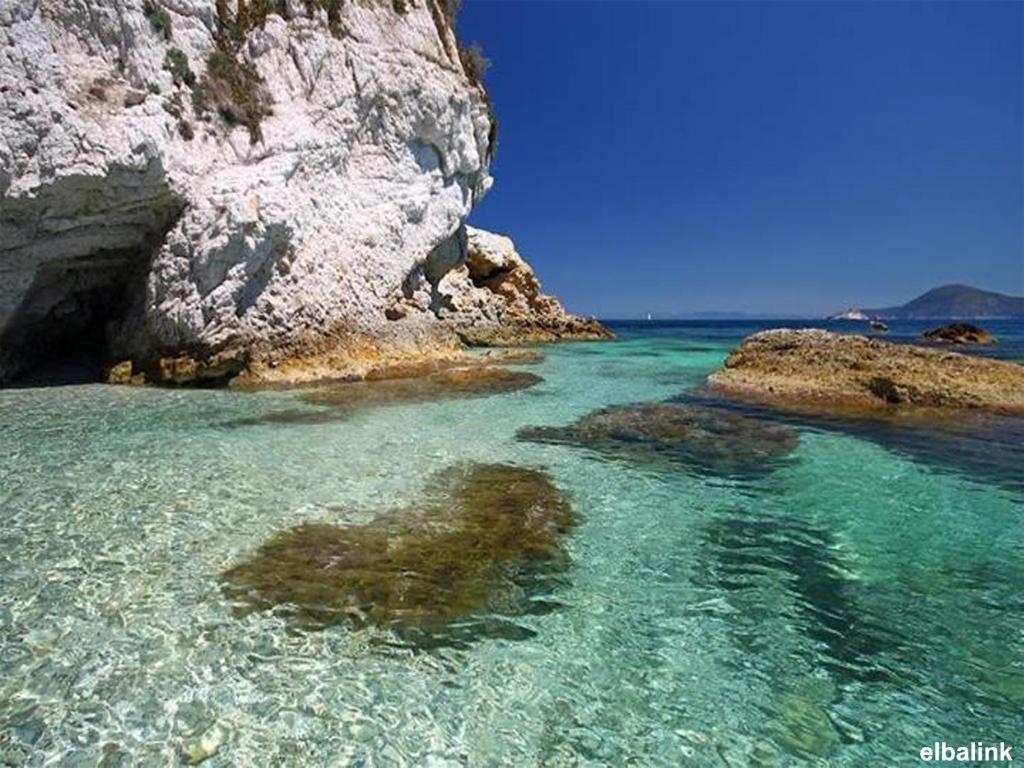 una spiaggia con acqua limpida e una grande roccia di Residence Capobianco a Portoferraio