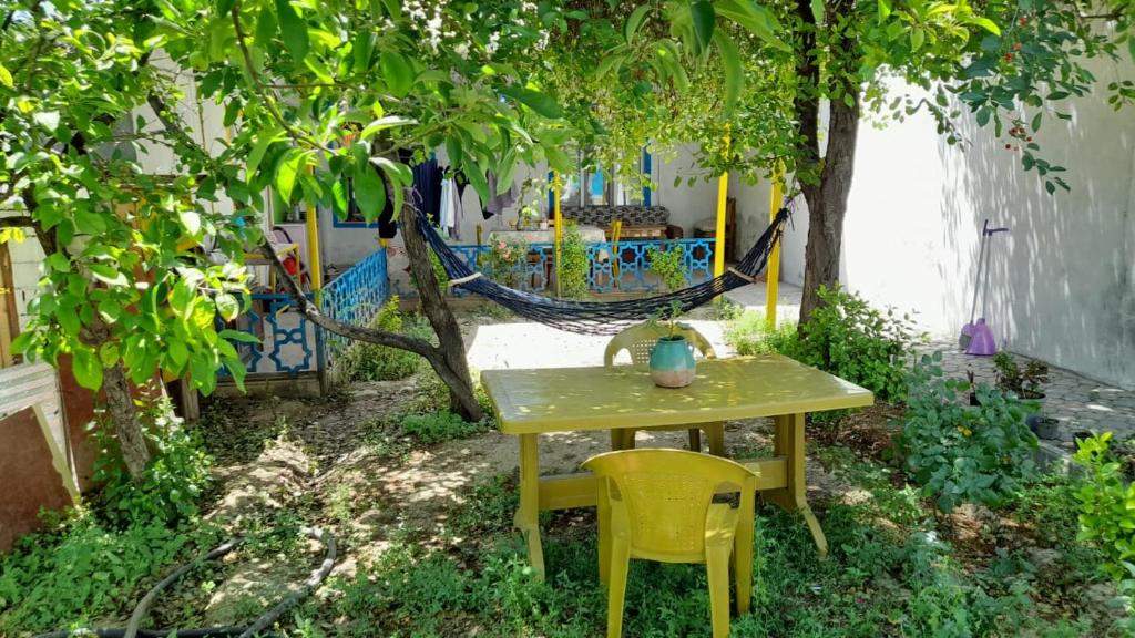 a yellow table and chairs in a garden with a hammock at Noa Hostel and Guest House in Naxçıvan