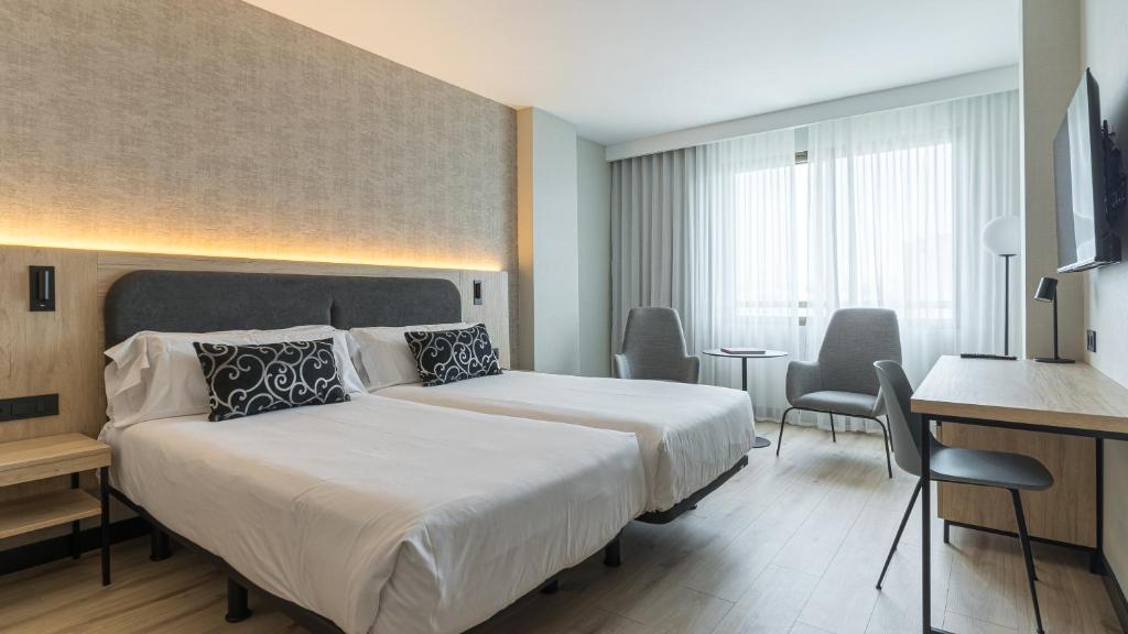 パンプローナにあるホテル ブランカ デ ナヴァラの大きなベッドとデスクが備わるホテルルームです。