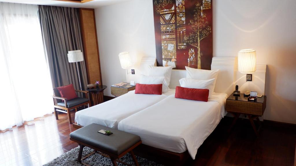 A bright twin room with two beds, red accent cushions and a large curtained window.