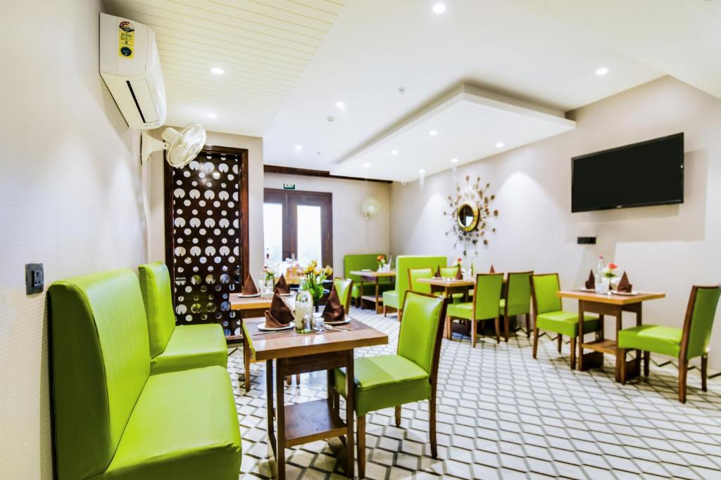 ニューデリーにあるHotel Bluestone - Nehru Placeの緑の椅子とテーブル、薄型テレビが備わるレストラン