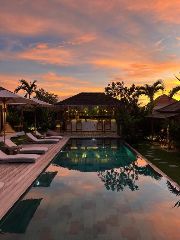 a swimming pool with lounge chairs and a sunset at EHOA BALI Nyanyi Boutique Hotel - In front of entrance to NUANU in Tanah Lot