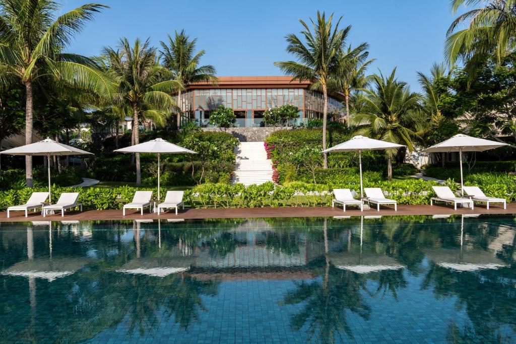 a pool with chairs and umbrellas in front of a building at Alma Resort Cam Ranh in Cam Ranh