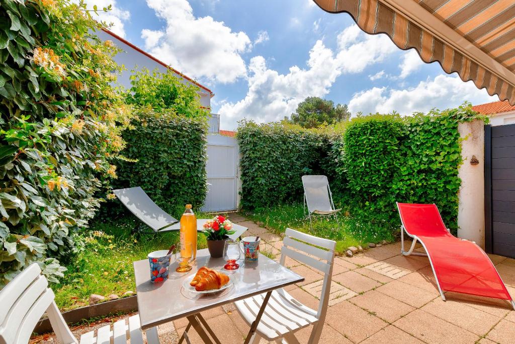 une terrasse avec une table, des chaises et une haie dans l'établissement Maison pour 6 proche plage, lac et zoo, à Les Sables-dʼOlonne