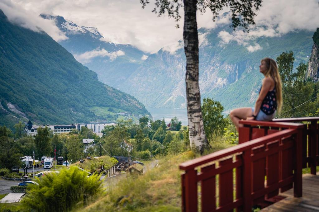 a woman sitting on a railing looking at a valley at Vinje Camping in Geiranger