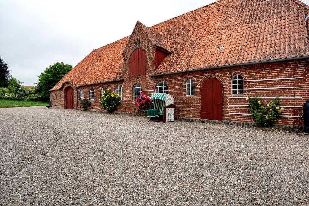 a red brick building with red doors and a gravel driveway at Ferienwohnung Landhaus Loose in Schashagen