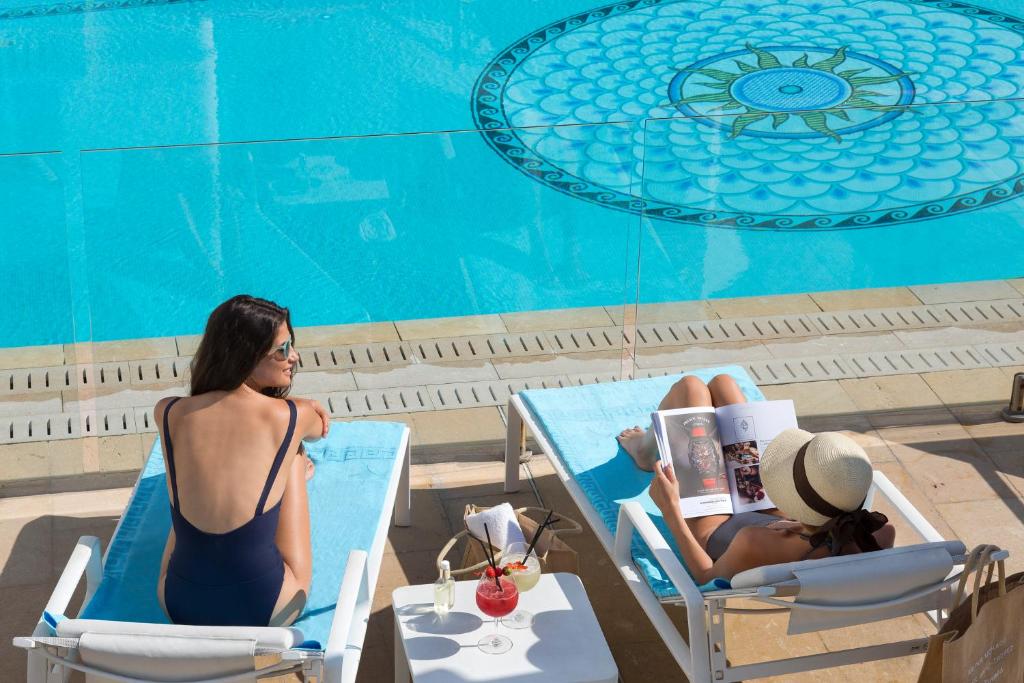 two women sitting in chairs next to a swimming pool at Hôtel Barrière Le Majestic Cannes in Cannes