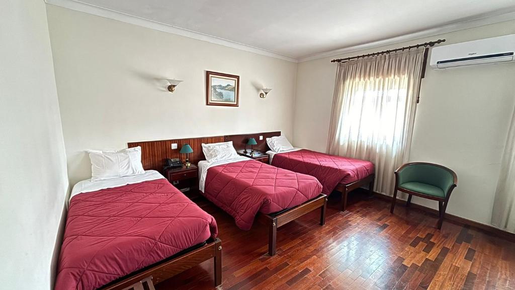 a hotel room with two beds and a chair at Hotel Trindade Coelho in Mogadouro