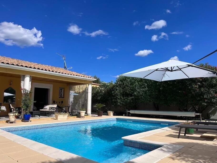 - une piscine avec un parasol à côté d'une maison dans l'établissement Belle villa avec piscine et spa, à Teyran