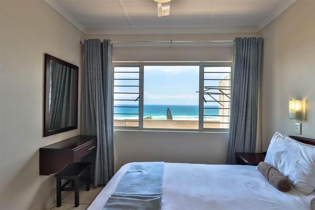 a bedroom with a bed and a window with a view of the beach at #16 Illovo Views in Kingsburgh