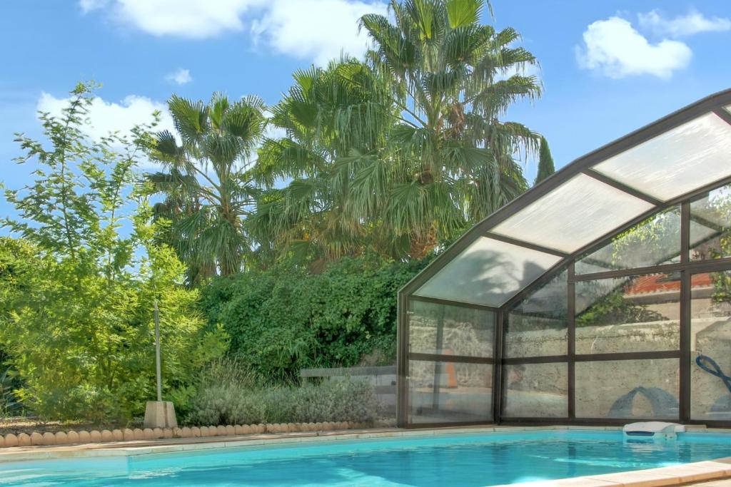 a swimming pool with a glass house and palm trees at Appartement d'une chambre avec piscine partagee jardin clos et wifi a Marseillan a 6 km de la plage in Marseillan