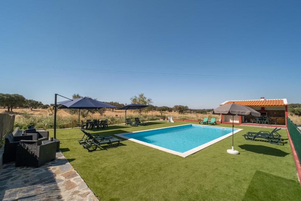 a pool in a yard with chairs and umbrellas at Casa da Ti Inácia - Praia Azenhas D El Rey in Montes Juntos