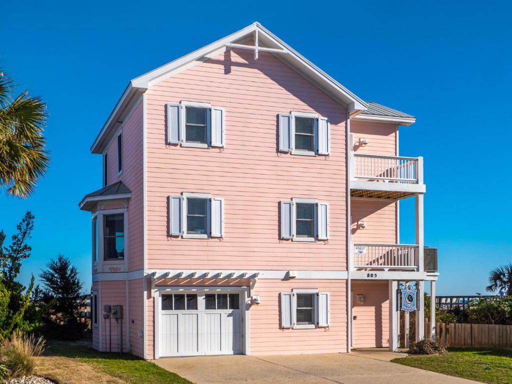 a pink house with white windows and a balcony at Over The Moon in Kure Beach