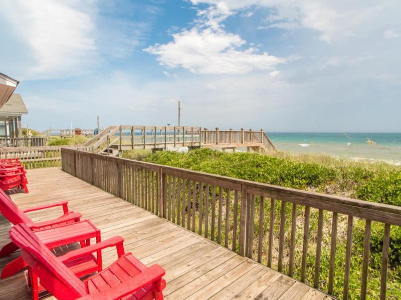 a deck with two red chairs and the beach at Pelican Perch in Surf City