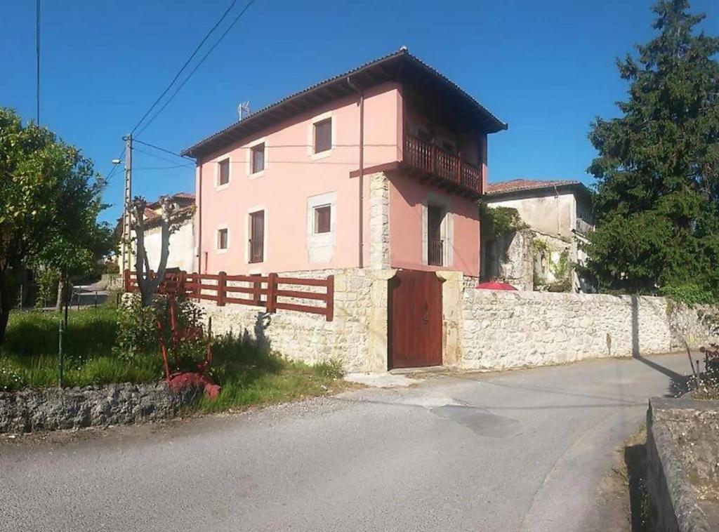 een roze huis met een hek aan de kant van de weg bij Casa vacacional La Coruxa in Vidiago