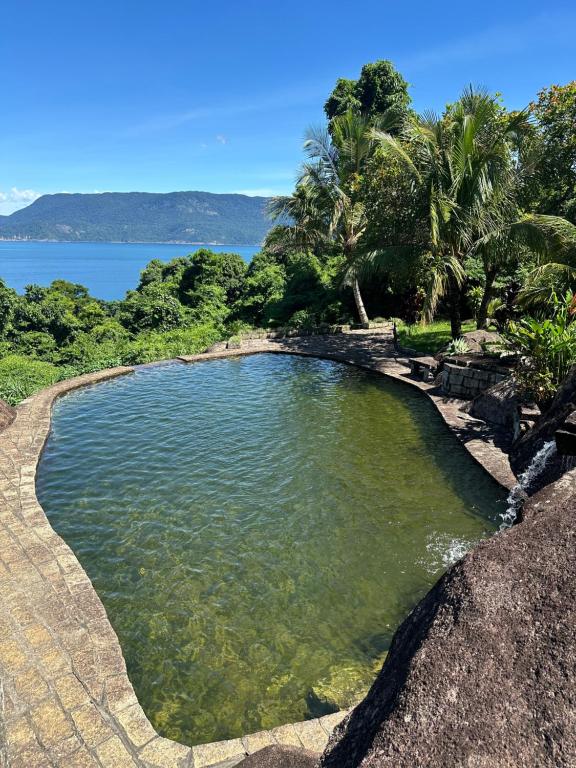una piscina de agua con palmeras y un cuerpo de agua en Ilhabela Chalés, en Ilhabela