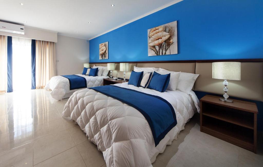 two beds in a hotel room with a blue wall at Port View Guesthouse in Marsaxlokk