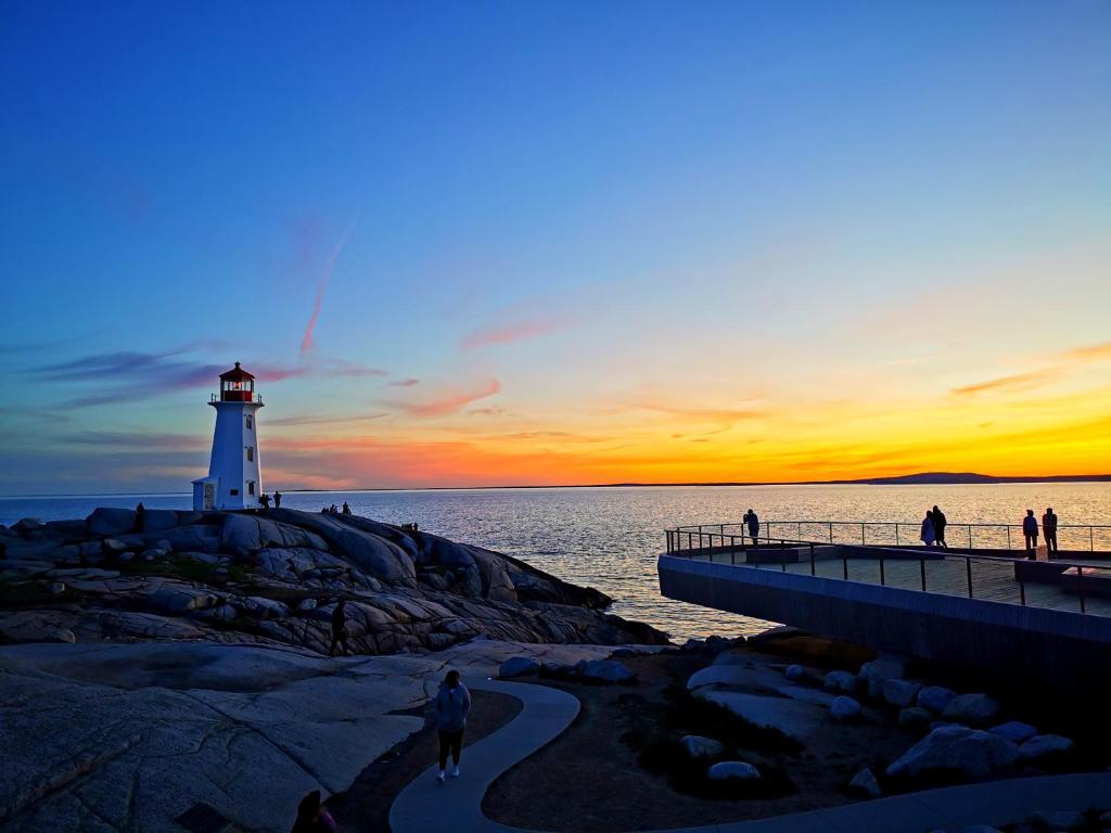 a lighthouse with people walking on a pier with the ocean at 181 Oceanside Inn in Peggy's Cove