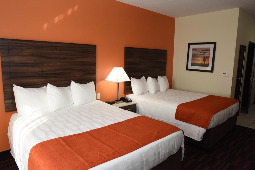 Home Away Kitchen Suites Enid في Enid: سريرين في غرفة الفندق بجدران برتقالية
