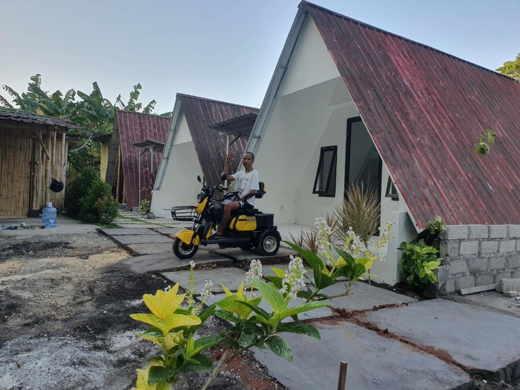 a man sitting on a scooter in front of a house at the bamboo Bali Cabin in Nusa Dua
