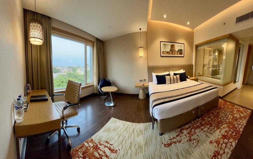 Habitación de hotel con cama, escritorio y ventana en The Fern Residency Sarnath en Varanasi