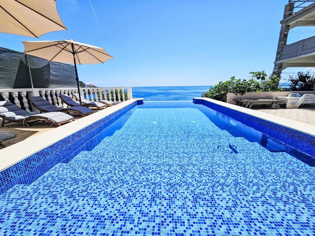 a blue swimming pool with chairs and an umbrella at Apartment Snježana-1 by Interhome in Zavalatica