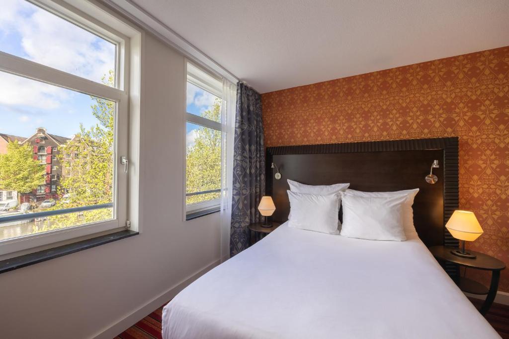 a bedroom with a white bed and two windows at Grand Hotel Amrâth Amsterdam in Amsterdam
