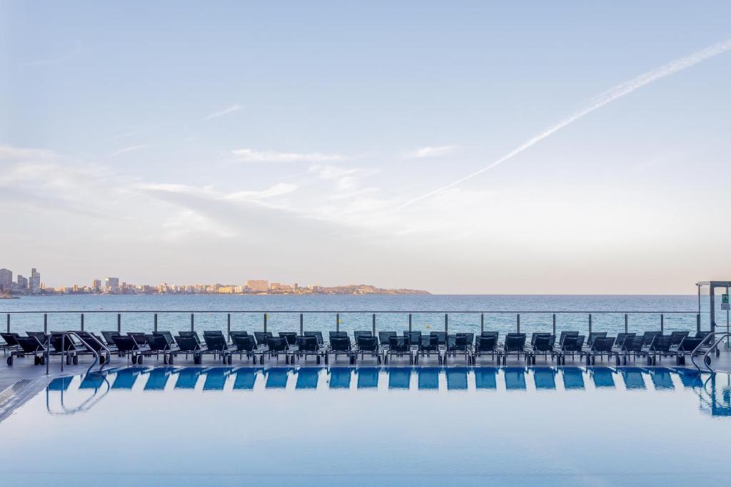 a pool with chairs and the ocean in the background at Melia Alicante in Alicante