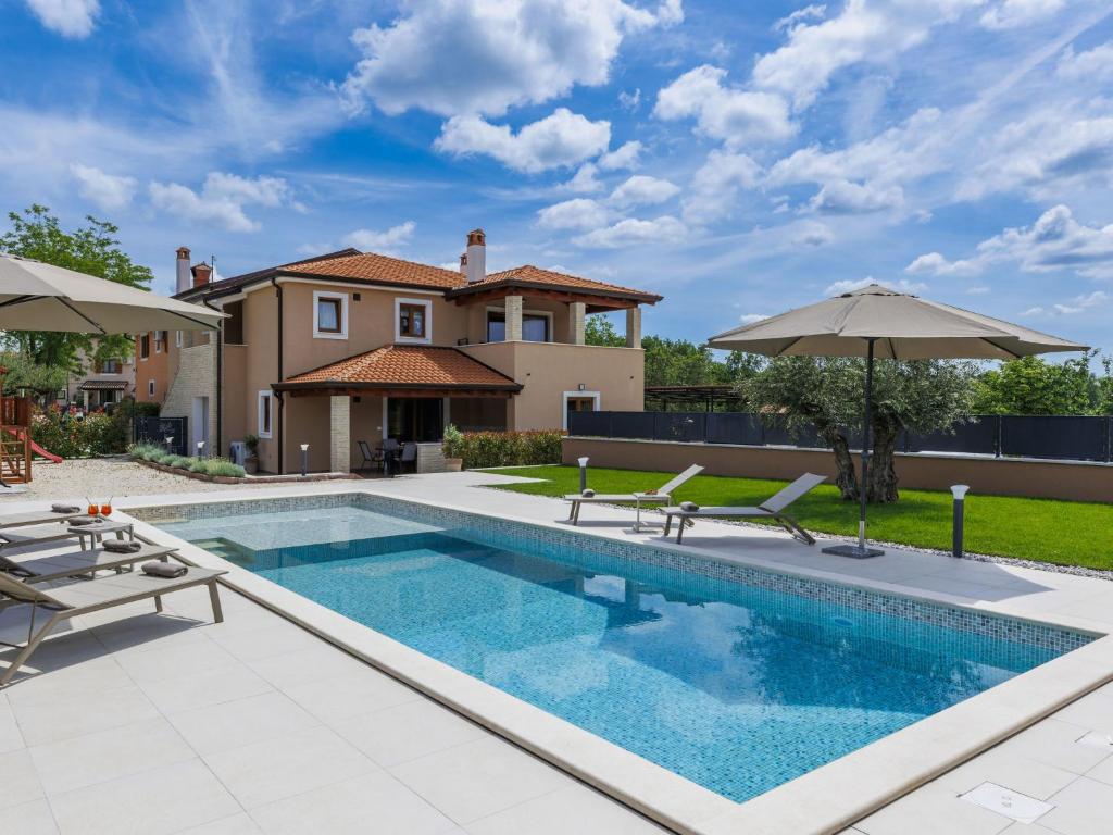a pool with chairs and umbrellas next to a house at Apartment Emili by Interhome in Vižinada