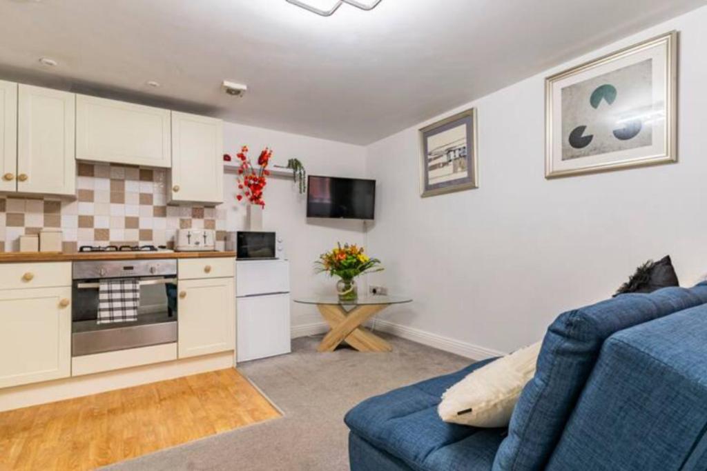 a living room with a blue couch and a kitchen at The Nook, Cosy 1BR in Blandford, Dorset in Blandford Forum