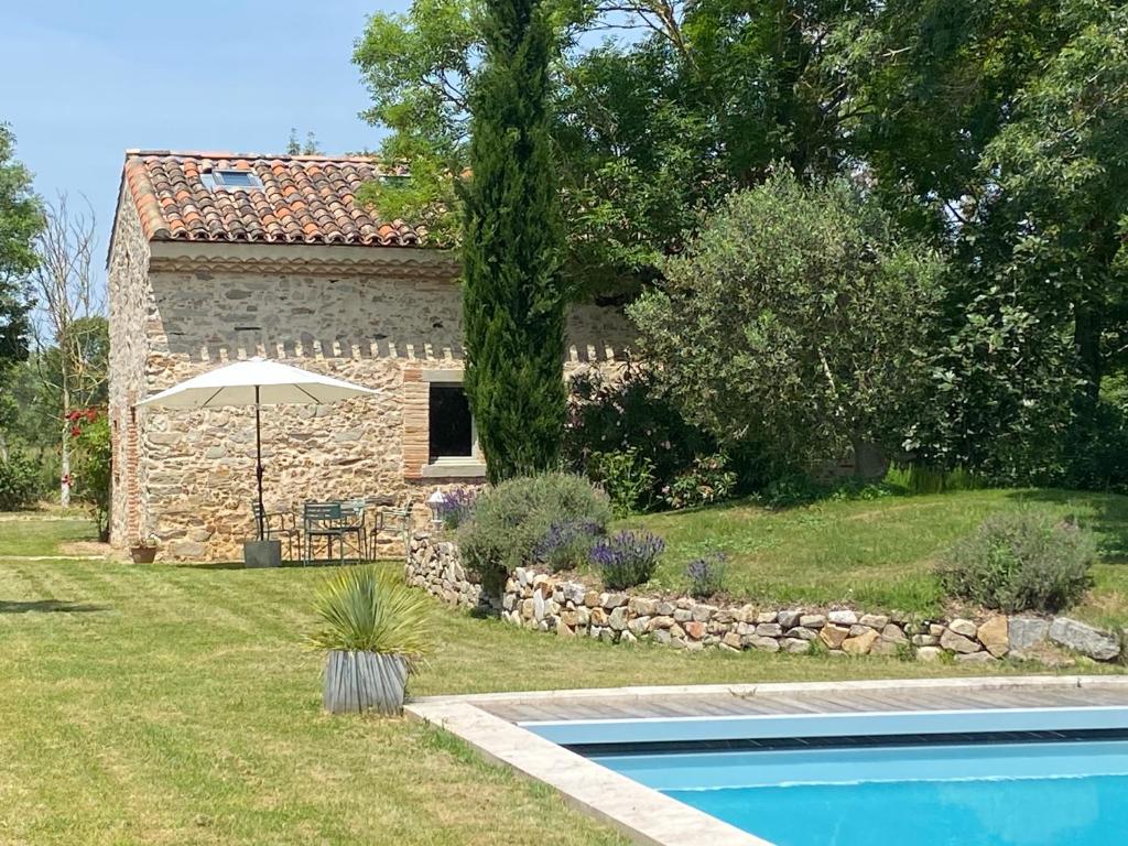 ein Steinhaus mit einem Pool und einem Sonnenschirm in der Unterkunft le Fournil de l'Albenque in Revel