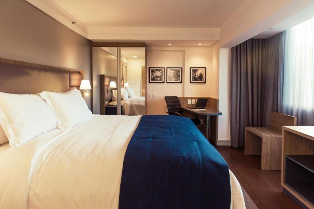 a hotel room with a large bed and a desk at Quality Porto Alegre in Porto Alegre