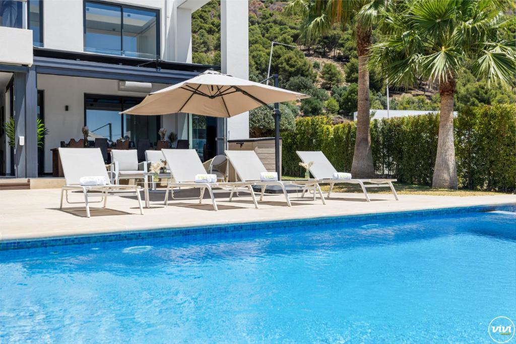 Un grupo de sillas y una sombrilla junto a una piscina. en ViVi Homes -Villa Yara Pool, Sauna, Spa & Garden, en Mijas