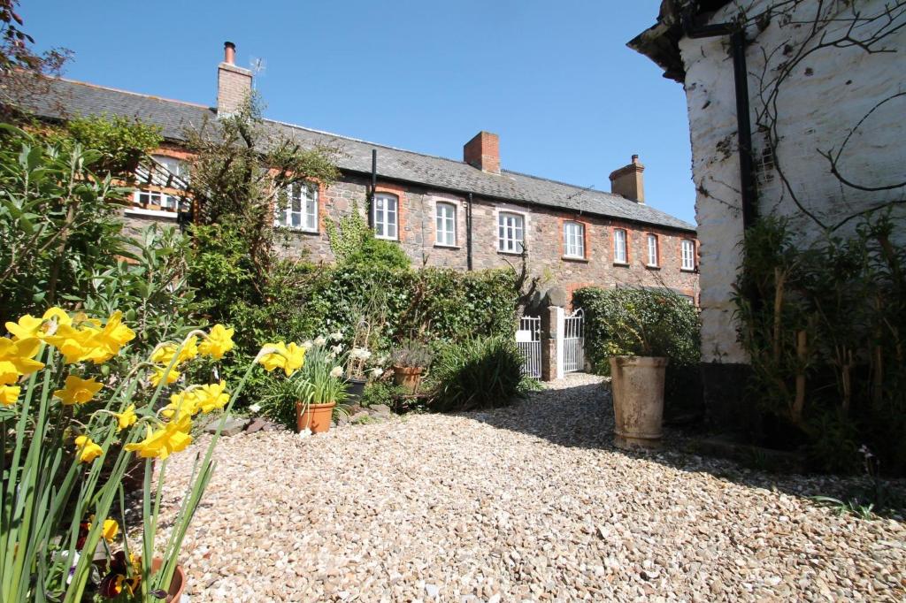 波洛克的住宿－Grace Cottage, Porlock，一座古老的砖房,前面有黄色的花