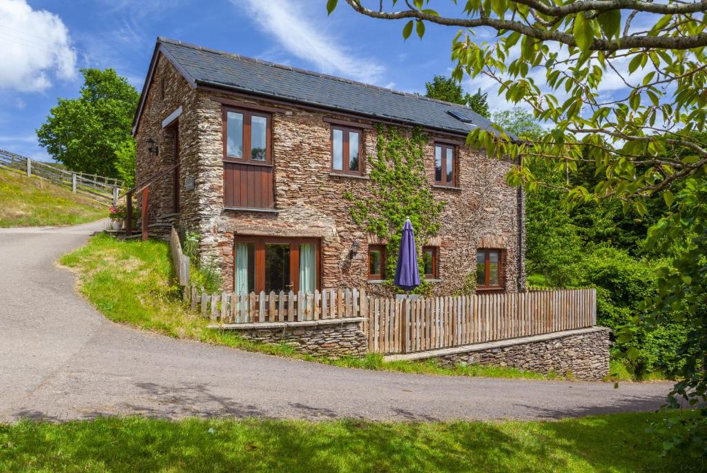 una casa de piedra con una valla y una sombrilla azul en The Granary, en Luxborough